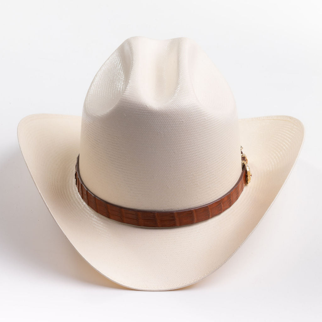 A cream-colored cowboy hat with a brown band and gold-colored decorative studs, photographed on a clean light gray background