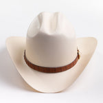 A cream-colored cowboy hat with a brown band and gold-colored decorative studs, photographed on a clean light gray background
