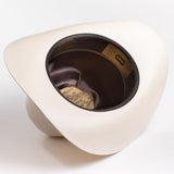 A cream-colored cowboy hat shown from an overhead angle, displaying its dark brown satin interior and a gold-toned badge insert