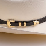 Close-up of a black textured hat band with gold-tone hardware and small red accents, shown wrapped around a cream-colored cowboy hat