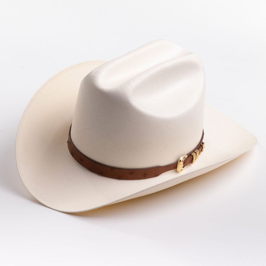 A cream-colored cowboy hat with a brown leather band and gold buckle, photographed on a clean light gray background