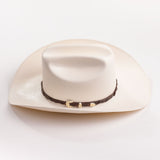 An off-white colored cowboy hat with a dark brown band and gold buckle, photographed on a clean white background