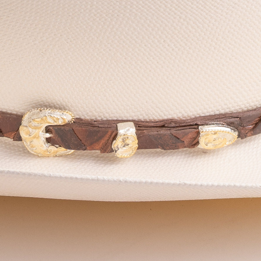 A close-up of a brown leather hat band with ornate gold-toned conchos, shown resting on a light cream-colored hat