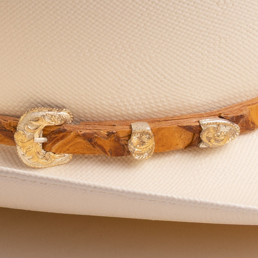 A closeup of an off-white colored hat with brown wood-like band with a gold and silver band