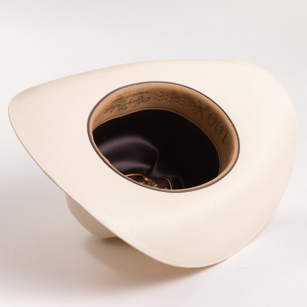 An off-white colored cowboy hat shown from a top-down angle, displaying its wide brim, dark interior, and tan inner band with embossed lettering