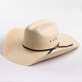 A light beige woven straw cowboy hat with a black ribbon band and a small silver buckle, photographed on a clean white background