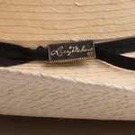 A close-up of a black ribbon hatband with a rectangular black label featuring gold cursive script that reads 'Larry Mahan' and a gold border, shown tied around a woven straw hat