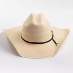 A light beige woven straw cowboy hat with a black ribbon band and a small silver buckle, photographed on a clean white background