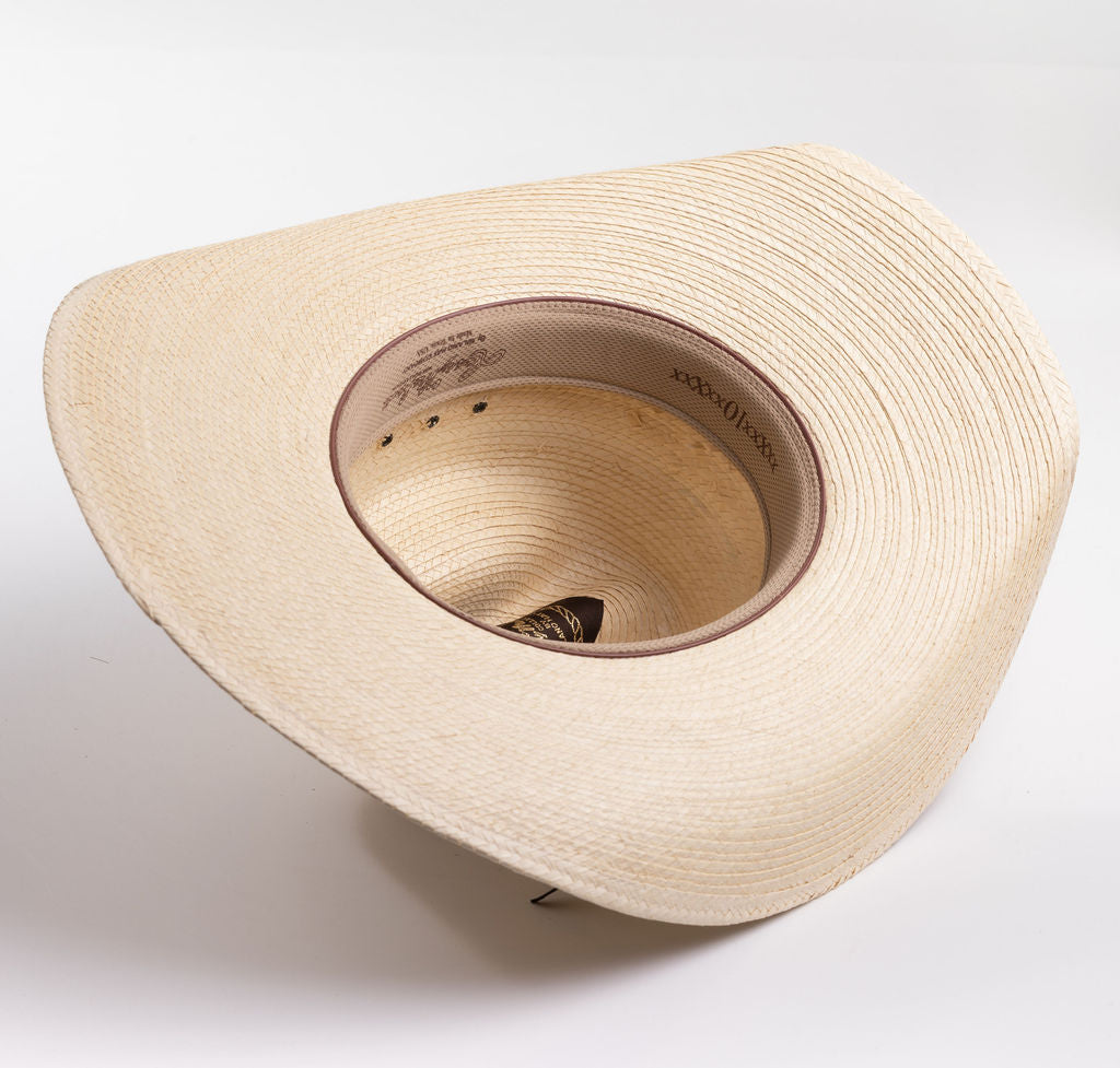 A light beige woven straw cowboy hat with a black ribbon band and a small silver buckle, photographed on a clean white background