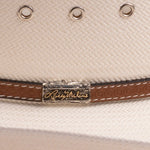 Close-up of an off-white cowboy hat featuring silver-tone eyelets and a brown leather band accented by a silver-toned metal logo plaque reading as 'Larry Mahan's'