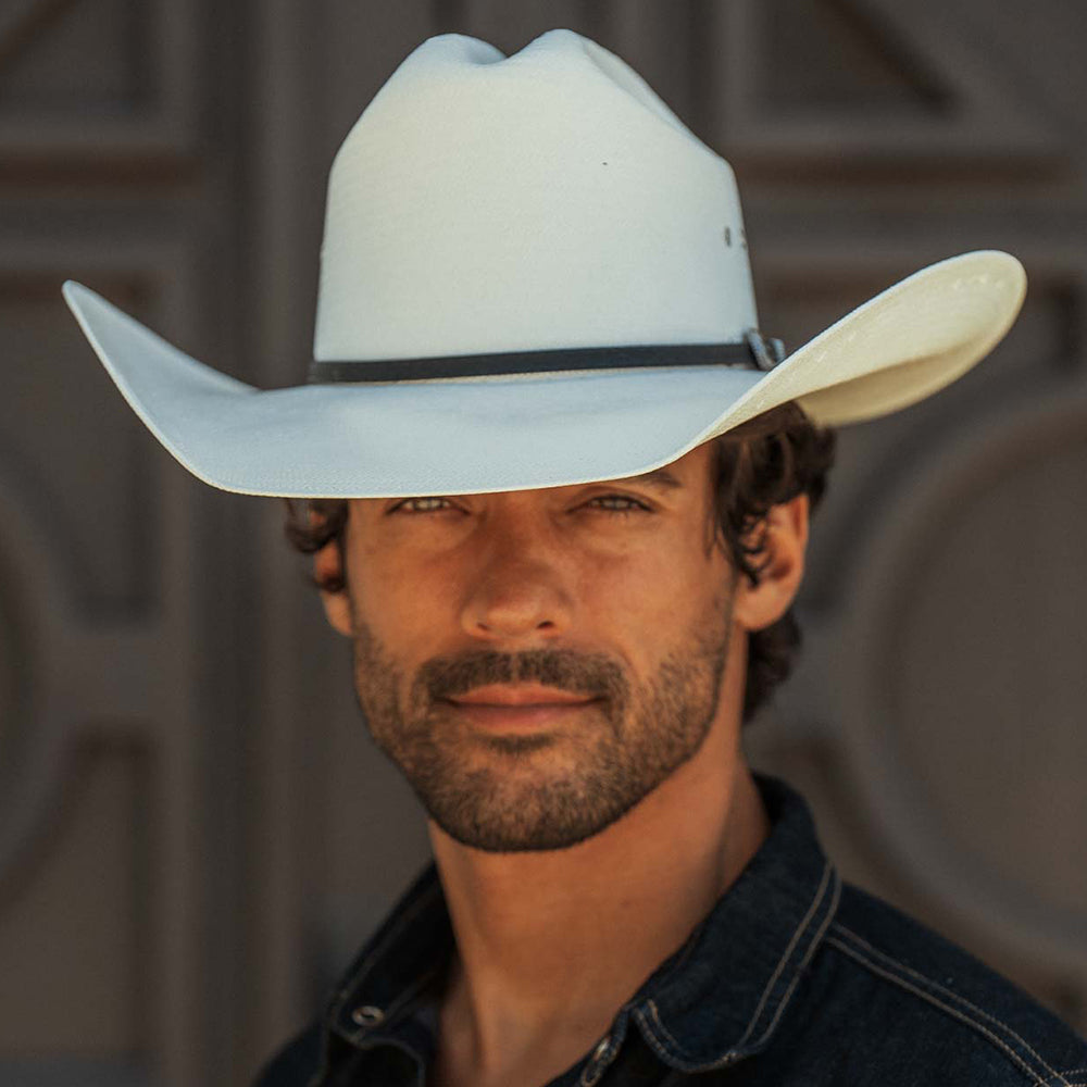 A man wearing a white cowboy hat with a black band and a dark denim shirt, shown in a close-up portrait