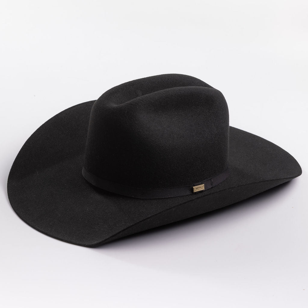 A black felt cowboy hat with a wide brim and a black band around the crown, featuring a small gold brand pin on the band, set against a clean light gray background.