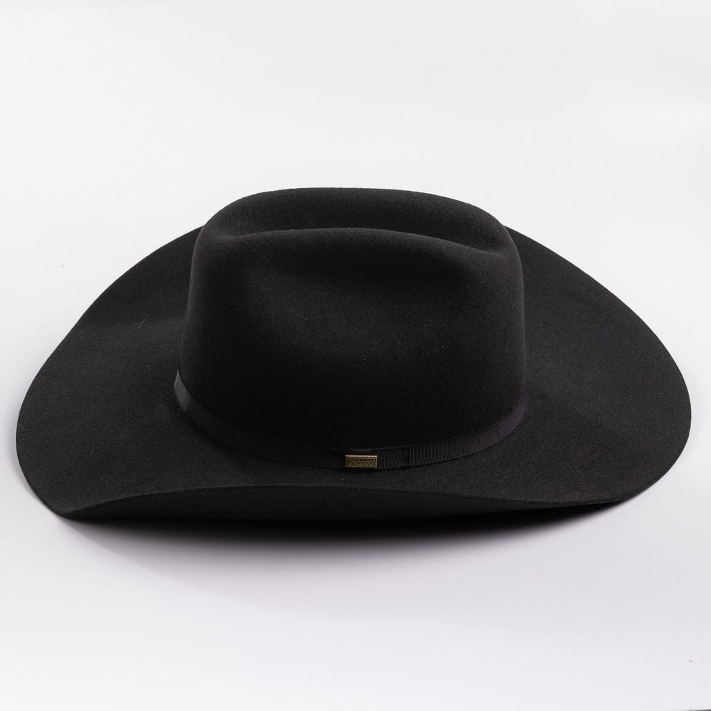 A black felt cowboy hat with a wide brim and a black band around the crown, featuring a small gold brand pin on the band, set against a clean light gray background.