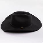 A black felt cowboy hat with a wide brim and a black band around the crown, featuring a small gold brand pin on the band, set against a clean light gray background.