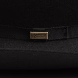 Close-up of a black felt hat with a black ribbon band and a small gold-tone metal pin engraved with "Worn by Legends"