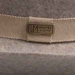 Close-up of a beige grosgrain ribbon band with a rectangular metal logo plate reading "Worn by Legends" on a gray felt hat