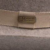 Close-up of a beige grosgrain ribbon band with a rectangular metal logo plate reading "Worn by Legends" on a gray felt hat