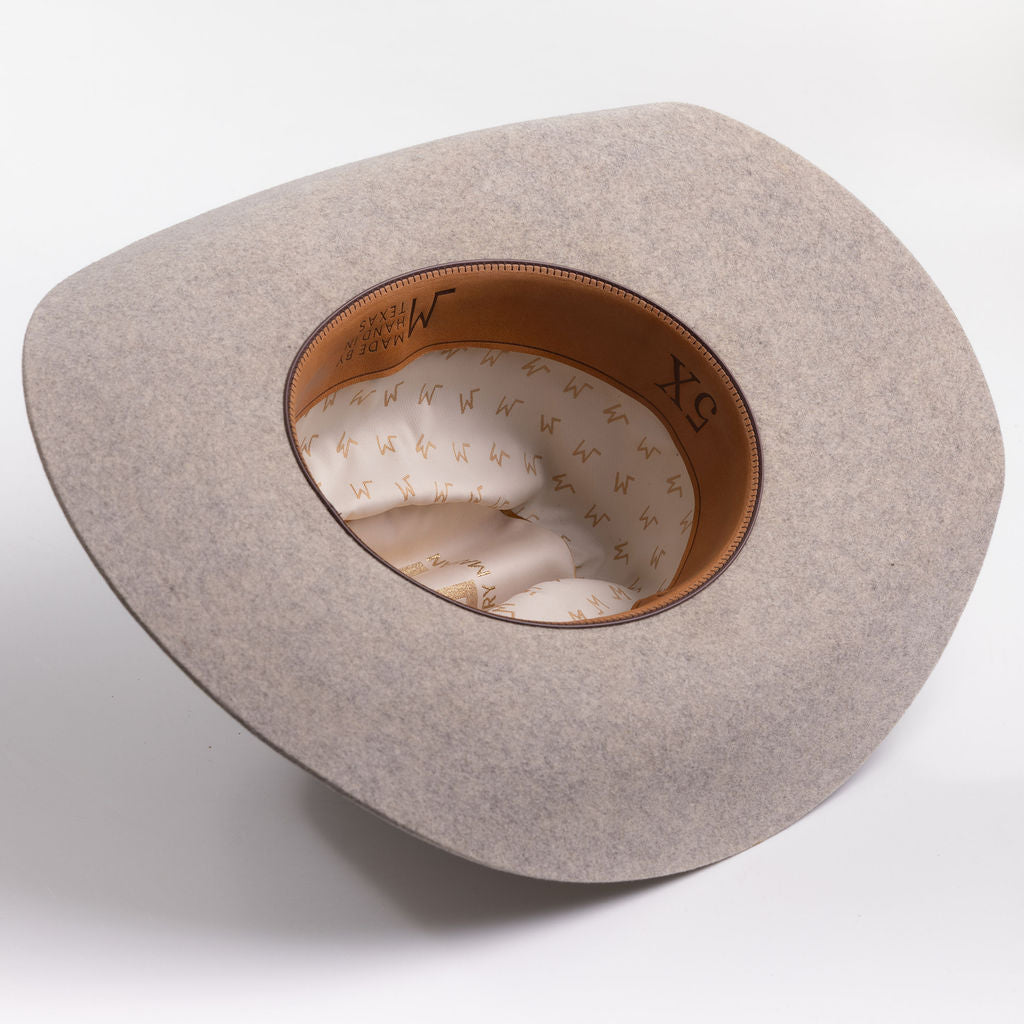 A light gray felt cowboy hat viewed from the inside, showing a tan leather inner band with black lettering and a cream patterned lining
