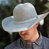 A man wearing a natural colored felt cowboy hat with a matching band, photographed outdoors with a blurred natural background.