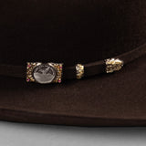 100X Independencia brown cowboy hat closeup of buckle with silver etched circle, gold edges, and red gems on each corner