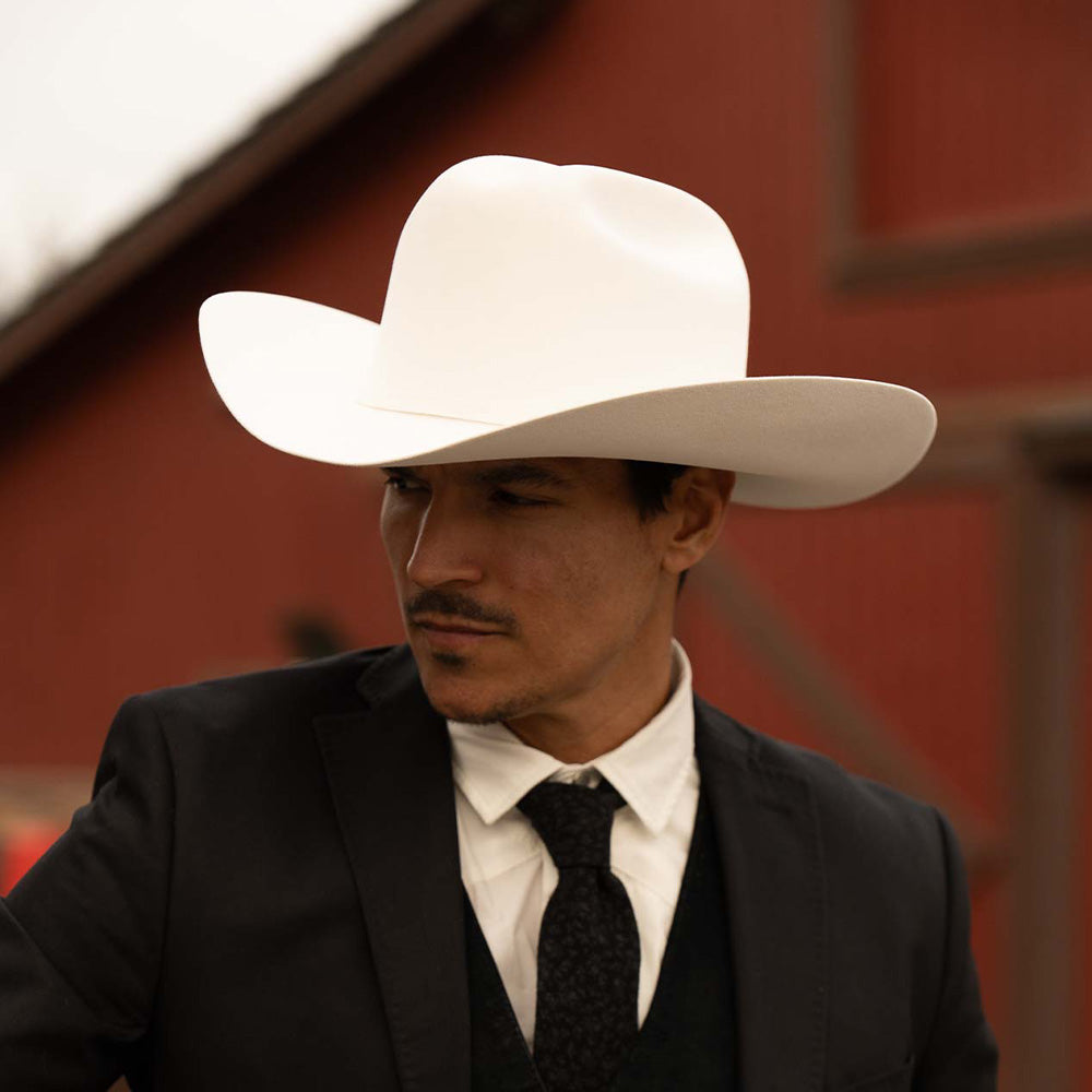 Man wearing a 1000X Imperial belly cowboy hat, a black jacket, vest, and tie, with a white shirt underneath, turning his head to the left
