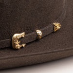 30X Opulento brown cowboy hat closeup of buckle in gold with small silver gems inlaid on the edges on a brown band