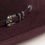 10X Jerarca black cherry cowboy hat closeup of buckle in black with silver and gold floral design with the letter L on a black cherry band