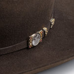 100X Independencia brown cowboy hat closeup of buckle with silver etched circle, gold edges, and red gems on each corner