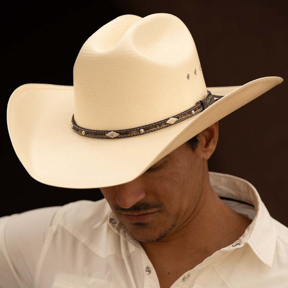 Man wearing a 10X Brindle brown cowboy hat with a white short sleeve shirt while looking downwards a little bit to the left