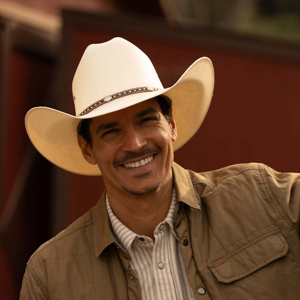 Smiling man wearing a 10X Bull ivory cowboy hat with a light brown jacket and white striped shirt