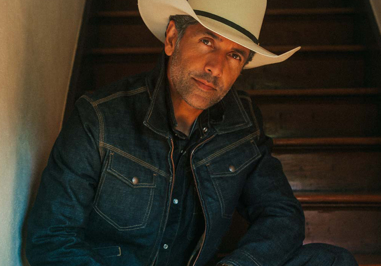 Man wearing a cowboy hat and denim jacket sitting on a wooden staircase.