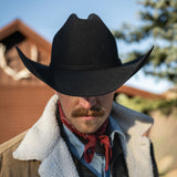 Person wearing a black cowboy hat and white shirt with a red bandana, outdoors.