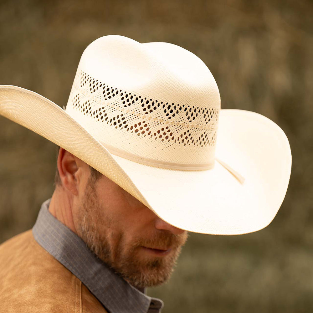 Bearded man wearing a 10X Durant ivory cowboy hat and dark tan vest with blue collar shirt looking downwards