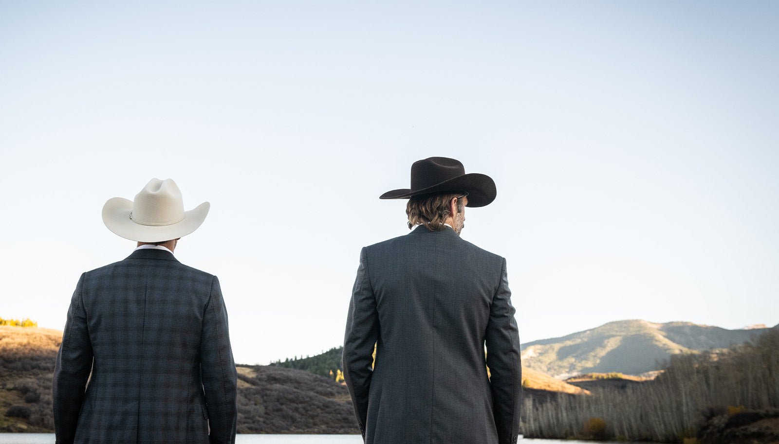 Two men in suits and hats standing in a desert landscape with mountains in the background.