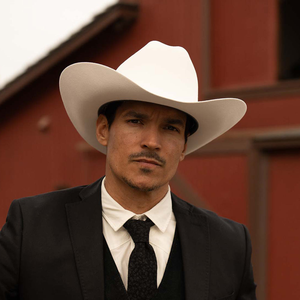 Man wearing a 1000X Imperial belly cowboy hat, a black jacket, vest, and tie, with a white shirt underneath