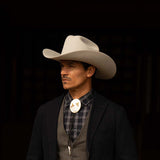 Man wearing a 100X Independencia belly cowboy hat with black jacket, grey shirt and vest, and silver bolo tie with gold horse riding emblems