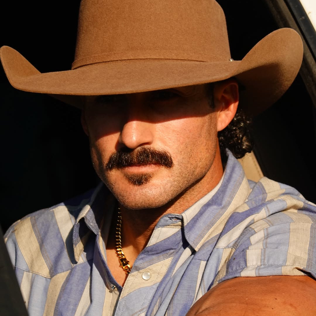 Man wearing a brown cowboy hat and striped shirt, sitting inside a car