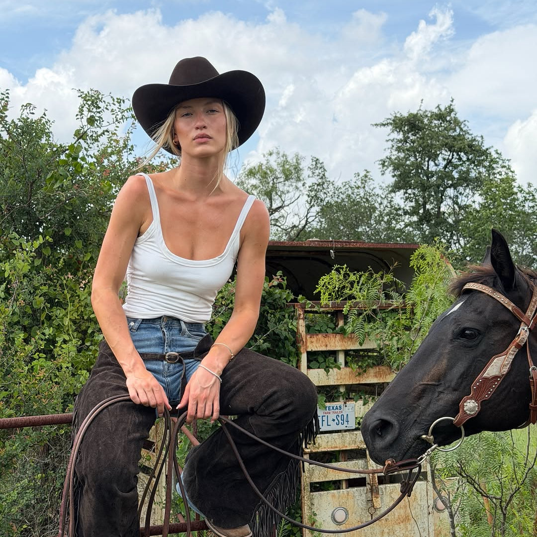 Woman in cowboy hat sitting on a horse with a rustic background
