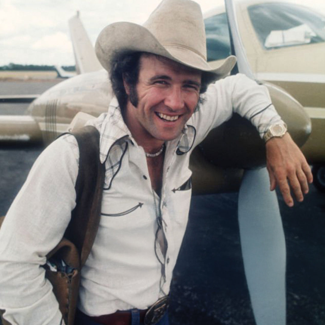 A young Larry Mahan in cowboy hat and white shirt leaning against a small airplane