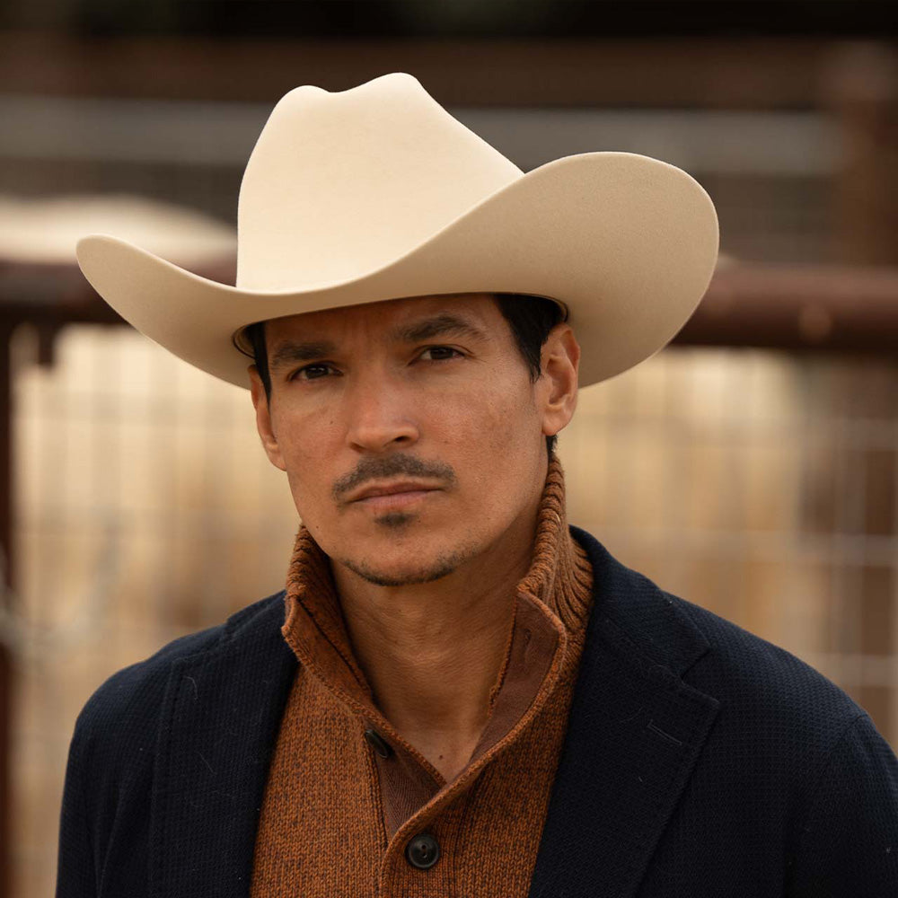 Man wearing a 10X Jerarca belly cowboy hat, blue jacket with brown sweater underneath with a high collar