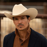 Man wearing a 10X Jerarca belly cowboy hat, blue jacket with brown sweater underneath with a high collar