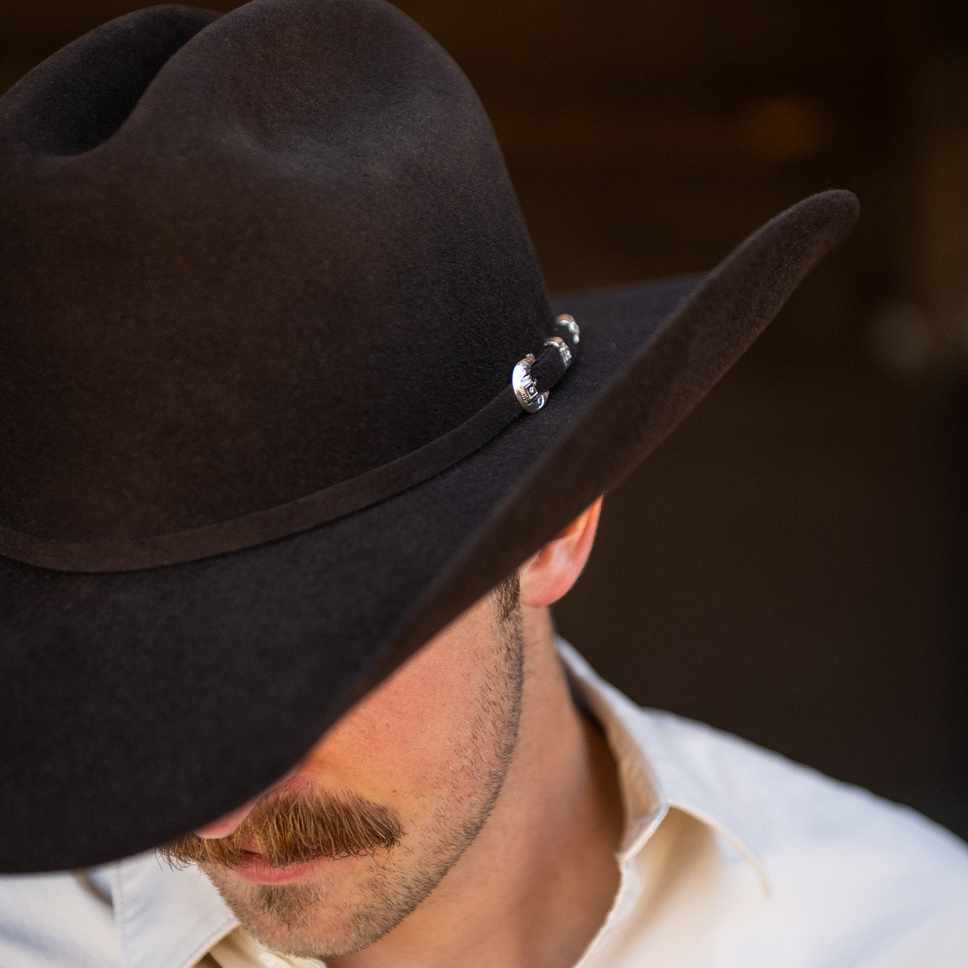 Man wearing a dark brown cowboy hat with a blurred background