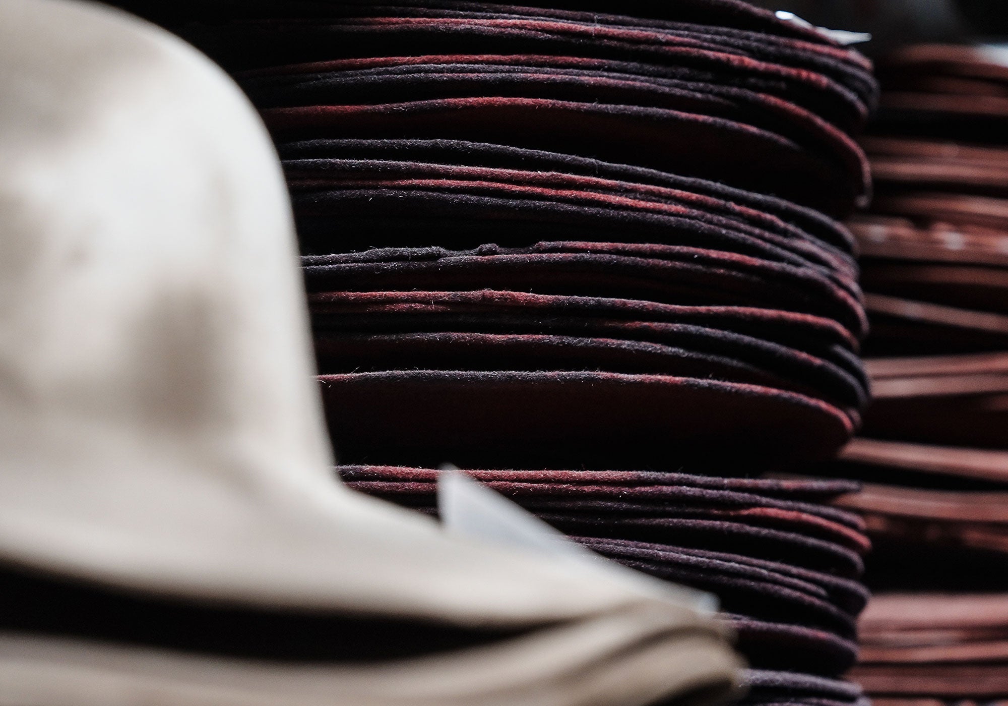 Stacks of dark red hat bodies in the background of a white stack of hat bodies