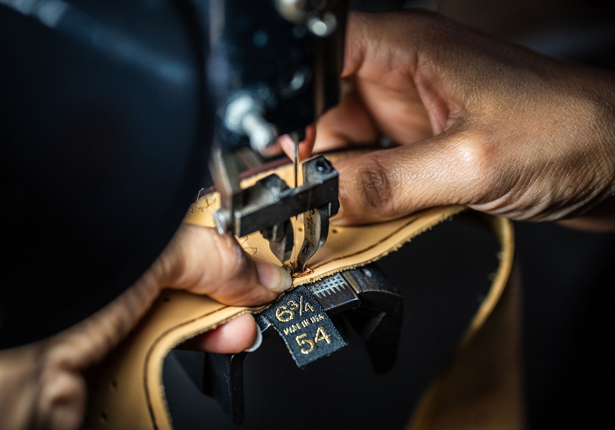 Woman using a machine to stitch a size label to the leather strap of a hat
