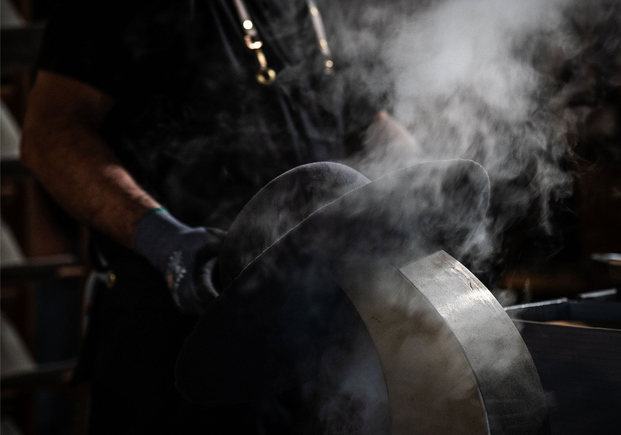 Black hat with steam rising up into it while a man with blue gloves holds it up to a machine's spout