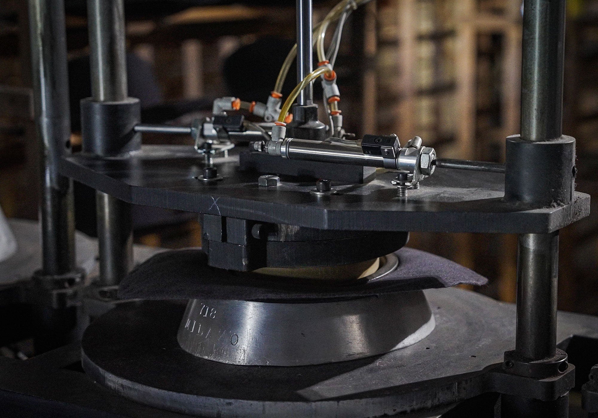 Black and silver colored machine with yellow tubes coming out of the top pressing a hat block into the underside of a hat