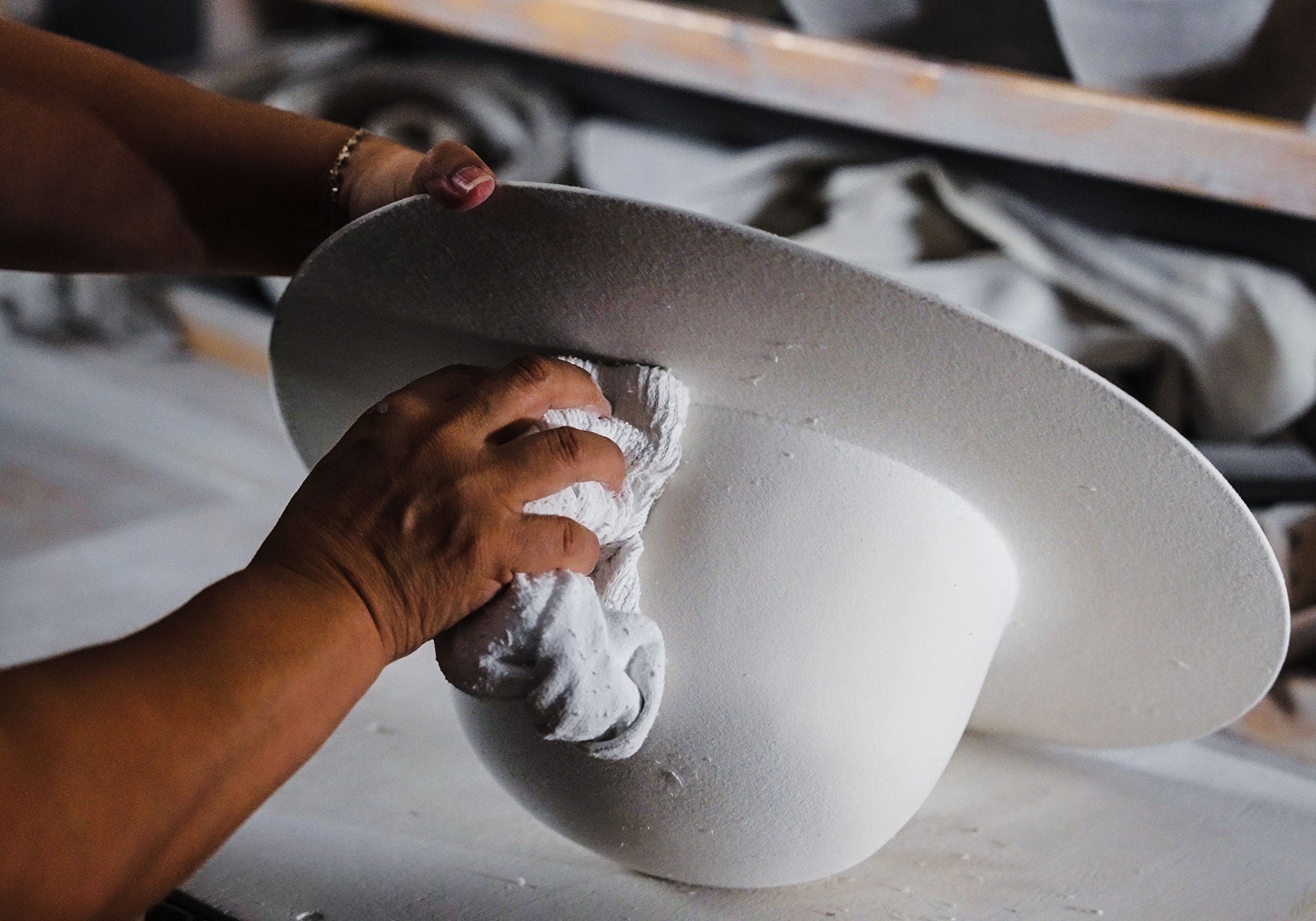 Woman adding pastel coloring to an upside down white hat with a cloth