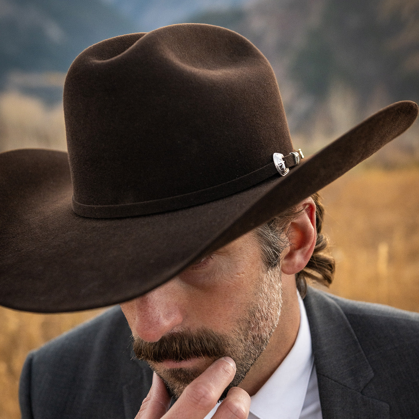 Man wearing a brown cowboy hat with a blurred natural landscape in the background