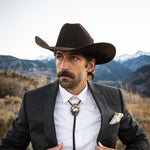Man wearing a cowboy hat and suit with a mountainous background