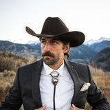 Man wearing a cowboy hat and suit with a mountainous background